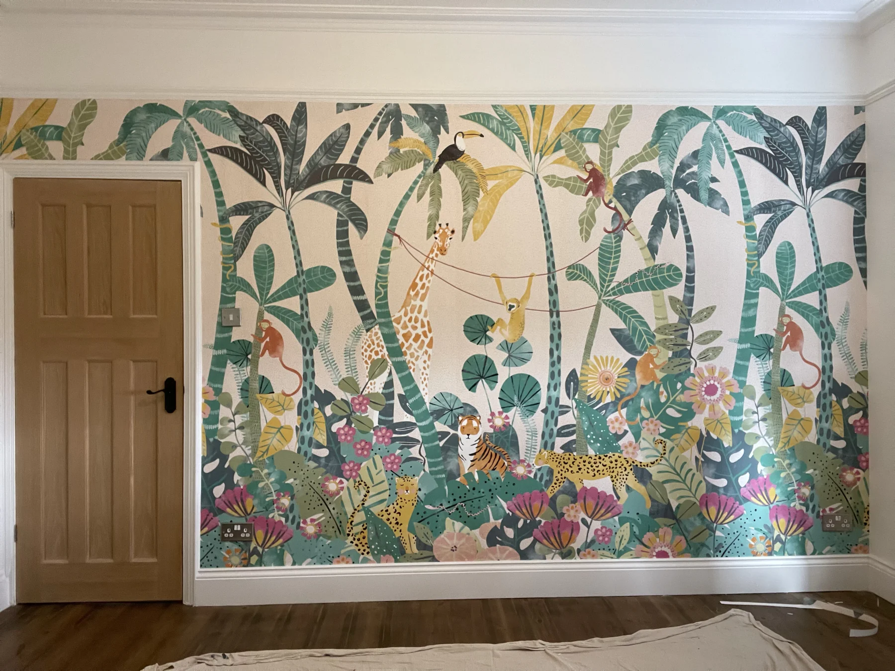 Botanical wallpaper mural installed across a bedroom wall with white skirting and a timber door