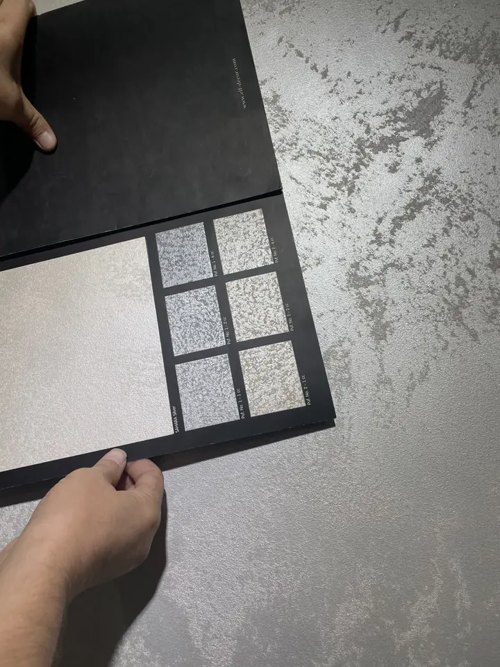 Polished plaster sample card held against a textured silver wall finish