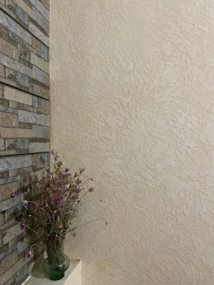 Textured plaster wall detail beside exposed brick and a vase of dried flowers